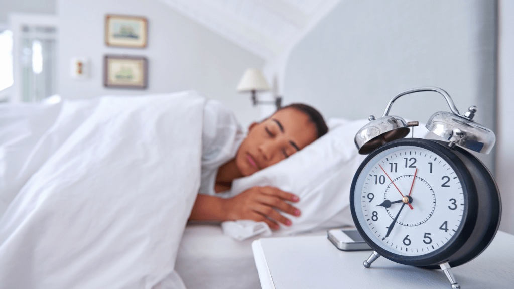 A person sleeping on a bed, there is a clock on a bedside table that is in focus